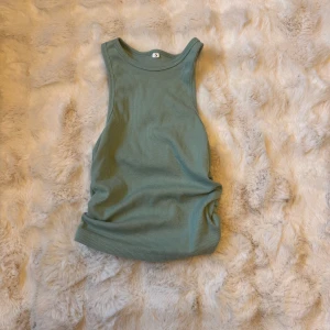 Ribbad grön linnetopp - Snygg ribbad linnetopp i en dämpad grön nyans. Modellen är ärmlös med breda axelband och rund halsringning. Perfekt att styla med jeans eller kjol för en chill look. Mjuk och stretchig känsla tack vare bomullsmaterialet.