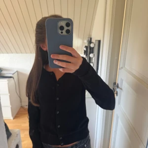 Svart kofta från H&M XS - En svart, klassisk kofta från H&M i storlek XS. Koftan har rund halsringning, långa ärmar och knäppning med svarta knappar framtill. 