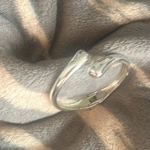 Silvrigt armband med öppningsfunktion - Snyggt armband i silverfärgad metall med rundad form och stilren design. Armbandet har en smart öppningsfunktion med gångjärn som gör det enkelt att ta på och av. Perfekt för dig som gillar minimalistiska accessoarer med en modern touch.
