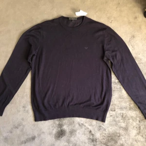 Svart tröja från Emporio Armani - Snygg mörkblå tröja från Emporio Armani med diskret logga på bröstet. Tröjan har rund halsringning, långa ärmar och är tillverkad i mjukt material som känns lyxigt mot huden. Perfekt för dig som gillar stilrena och klassiska plagg.