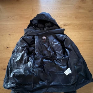 Svart dunjacka från Canada Goose - Säljer en svart dunjacka från Canada Goose med huva och klassisk logga på ärmen. En defekt på fickan men går att fixa överallt hemma eller i butik. Det är en äkta canada goose och allmänt riktigt fet