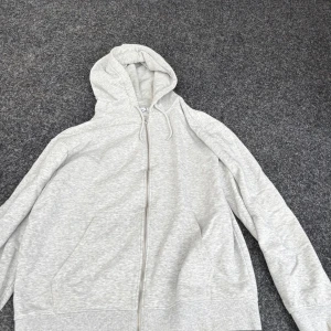 Ljusgrå hoodie från Weekday, M - Ljusgrå hoodie från Weekday i mjuk bomullsblandning. Klassisk modell med dragkedja, huva med snörning och två fickor framtill. Perfekt för chill dagar eller när du vill ha en enkel och clean look.