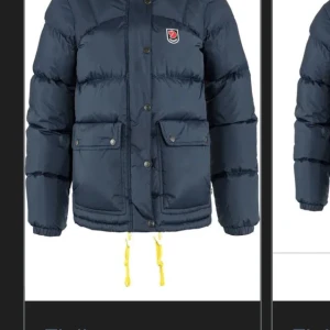 Mörkblå pufferjacka från Fjällräven - Säljer en mörkblå pufferjacka från Fjällräven med huva, gula snören och stora fickor framtill. Jackan har knappar och dragkedja, samt klassisk Fjällräven-logga på bröstet. Perfekt för kalla dagar och riktigt snygg till jeans. Endast använd under 1 vinter och ingen defekt. 