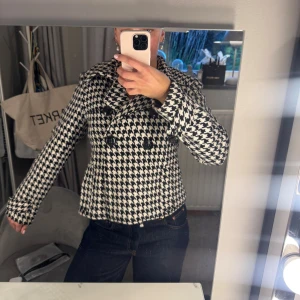 Svartvit rutig skepparkavaj - Säljer en snygg skepparkavaj i svartvitt hundtandsmönster. Jackan har dubbelknäppning med stora svarta knappar, klassisk krage och lång ärm. Jackan passar perfekt nu till hösten. Några knappar är lösa men det är bara att sy fast💖
