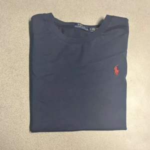 Mörkblå t-shirt från Polo Ralph Lauren - Snygg mörkblå t-shirt från Polo Ralph Lauren med klassisk röd broderad logga på bröstet. Tröjan är nästintill ny, det finns inga tecken på att den är använd. Hör av er vid frågor!