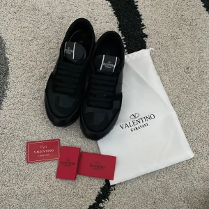 Svarta Valentino Garavani sneakers - Snygga svarta sneakers från Valentino Garavani med diskret camouflagemönster och klassisk snörning. Skorna har en chunky sula och är tillverkade i en mix av skinn och syntetmaterial. Perfekta för dig som vill ha en stilren och exklusiv look. Priset kan självklart sänkas vid snabb affär! Skriv vid funderingar!! Skorna kommer med det i bilderna men tyvärr inte box.