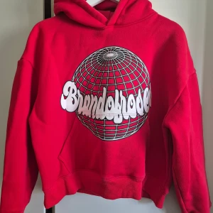 Röd hoodie Brandofroses croppad M - Snygg röd hoodie från Brand of roses i boxig, croppad passform. Tillverkad av mjuk bomullsfleece med dubbelfodrad huva och stort grafiskt tryck framtill. Perfekt för dig som gillar streetwear och vill sticka ut med cool design och skön komfort.