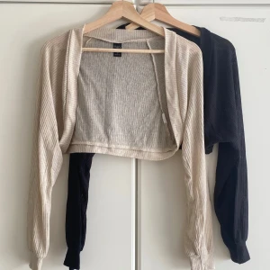 2 croppade koftor från Dazy, svart & beige - Två croppade koftor från Dazy, en i svart och en i beige. Båda är ribbade med lång ärm och öppen framtill. Perfekta att slänga över ett linne eller klänning för en chill look. Tunn och mjuk kvalitet som känns skön mot huden. 100 kr för båda eller en för 60kr