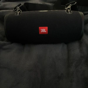 JBL Xtreme 2 - JBL Xtreme 2 bärbar Bluetooth-högtalare i svart, med original axelrem och laddare. Högtalaren är i fint skick utan synliga skador eller slitage. Perfekt för både inomhus och utomhusbruk med kraftfullt ljud och lång batteritid.