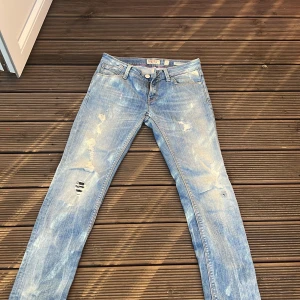 Replay Rockxanne ljusblå jeans - Snygga ljusblå jeans från Replay, modell Rockxanne. Jeansen har slitna detaljer och broderad Replay-logga med ros på bakfickan. Klassisk femficksmodell med raka ben och låg midja. Perfekta för en avslappnad streetstil.