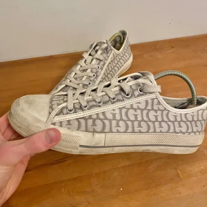 Beige sneakers från Guess med monogram - Snygga sneakers från Guess med tydligt monogrammönster över hela skon. Klassisk låg modell med snörning och rund tå. Ovandel i textil och sula i gummi. Perfekta för dig som gillar stilrena men ändå statement skor.