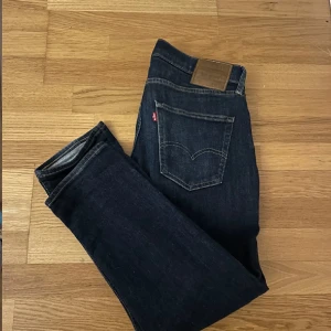 Levi's Premium mörkblå jeans straight - Mörkblå Levi's Premium jeans med klassisk femficksdesign och raka ben. Snygga kontrastsömmar och läderpatch bak i midjan. Jeansen är tillverkade i slitstarkt denim och har en tidlös look som passar till det mesta.