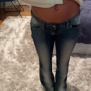 Cheap Monday blå bootcut jeans - Säljer ett par blå jeans från Cheap Monday med bootcut-snitt och låg midja. Jeansen har klassisk femficksdesign, slitningar och ljusa partier framtill för en cool, använd look. Materialet är jeans i bomull med lite stretch för skön passform.