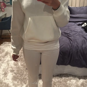 Vita yogabyxor från Gina Tricot - Säljer en vita yoga pant från Gina Tricot med klassisk känguruficka och huva. en relaxed passform, perfekt för chill dagar. Tillverkad i mjuk bomullsblandning som känns skön mot huden.