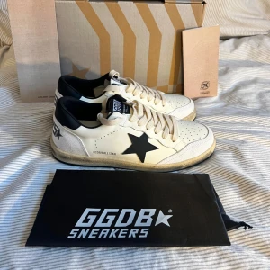 Golden Goose Ball Star sneakers, vit/svart  - Golden Goose Ball Star sneakers i vitt skinn med svart stjärndetalj på sidan och svart häl. Klassisk låg modell med perforerad tå, beige snörning och slitna detaljer på sulan för en cool vintagekänsla. Obs lnt 0rglnal. Box medföljer ej