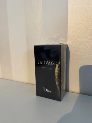 Dior Sauvage Eau de Parfum - Säljer en Dior Sauvage Eau de Parfum i elegant svart förpackning med vit text och klassisk Dior-logga på toppen. Kartongen är rektangulär och har en lyxig känsla, perfekt för dig som gillar exklusiva dofter.