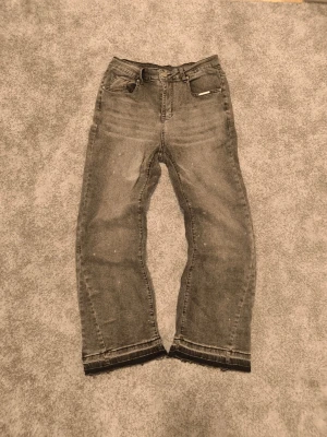 Grå flared jeans - Säljer ett par grå flared jeans med rak passform och rå, fransig kant nedtill. Jeansen har klassisk femficksdesign och en avslappnad vibe. Perfekta för dig som gillar en lite mer edgy stil.