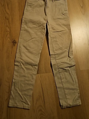 Beige chinos från Crocodile Wear - Snygga beige chinos från Crocodile Wear med klassisk rak passform. Byxorna har bälteshällor, knapp och dragkedja i gylfen samt två fickor fram. Perfekta för en clean och avslappnad stil. Använd 1 gång.