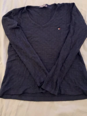 Mörkblå långärmad topp Tommy Hilfiger - Mörkblå långärmad topp från Tommy Hilfiger med v-ringning och diskret logga på bröstet. Tunn och mjuk kvalitet, perfekt för lager-på-lager. Klassisk och stilren design som funkar till det mesta.
