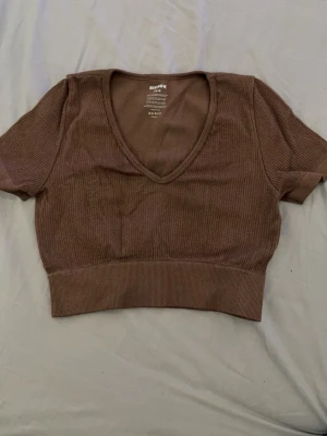 Brun ribbad croppad topp BikBok - Säljer en brun ribbad croppad topp från BikBok med v-ringning och korta ärmar. Toppen är i stretchigt material med snygg passform, perfekt till jeans eller kjol. Materialet är en mix av polyamid och elastan för extra komfort.