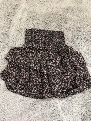 Svart och rosa blommig volangkjol - En svart volangkjol med ett gulligt rosa blommig mönster. Storlek 158-164 ifrån KappAhl. Använd några gånger och i ett bra skick.💗