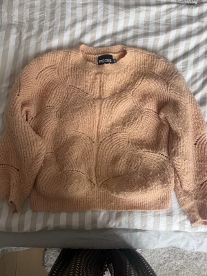 Orange stickad tröja från Pieces - Mysig orange stickad tröja från Pieces med rund halsringning och unikt vågigt mönster. Tröjan har långa ärmar och ribbade muddar vid ärmslut och nederkant. Perfekt för lager på lager och ger en avslappnad men trendig look.