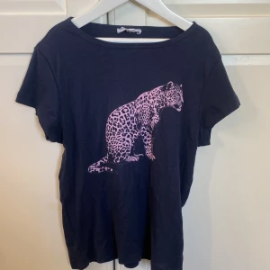 Svart t-shirt med leopardtryck Subdued - Mörkblå t-shirt från Subdued i mjuk bomull med korta ärmar och en stor rosa leopard på framsidan. Klassisk passform och rund halsringning. Perfekt för dig som vill sticka ut med ett coolt djurmotiv.