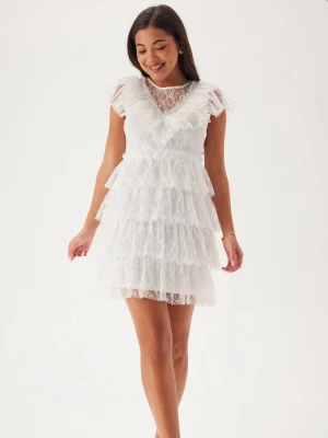 Studentklänning  - Superfin vit kort klänning i spets med flera lager volanger och v-ringad hals. Klänningen har ärmlös design och romantiska detaljer som ger en drömmig look. Perfekt för sommarens alla tillfällen.