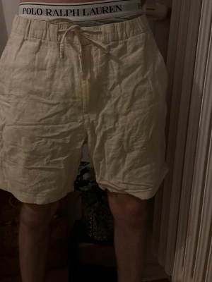 Beige linneshorts med snörning - Luftiga beige shorts i linne med snörning i midjan och avslappnad passform. Shortsen har elastisk midja och en bakficka. Perfekta för varma dagar och enkel stil. Hör gärna av dig vid frågor eller liknande🙏