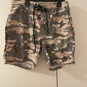 Camo badshorts, herr storlek L - Säljer ett par camouflagemönstrade shorts från WA med snörning i midjan. Shortsen har en relaxed fit och elastisk midja för extra komfort. Perfekta för sommaren och riktigt snygga till en enkel t-shirt. Storlek L