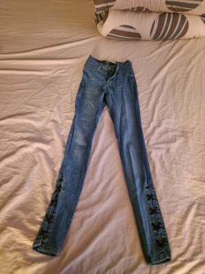 Blå skinny jeans med snörning - Snygga blå skinny jeans med cool snörningsdetalj längs nedre delen av benen. Jeansen har hög midja och klassisk femficksdesign. Perfekta för dig som vill ha en trendig och unik look.