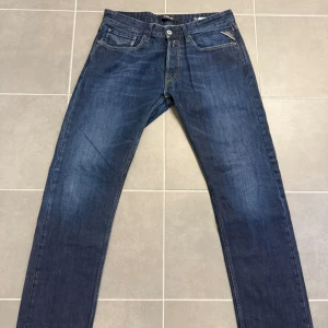 Blå Replay jeans straight fit - Snygga blå jeans från Replay med klassisk femficksmodell och raka ben. Jeansen har en mörk tvätt med subtila slitningar och detaljerade sömmar. Perfekta för dig som gillar en tidlös och clean stil.