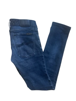 Mörkblå Nudie Jeans  - Snygga mörkblå  Nudie Jeans med klassisk femficksdesign och smal passform. Jeansen är tillverkade i stretchig bomullsdenim för en cool look. Perfekta för dig som gillar en tight siluett och stilren design.