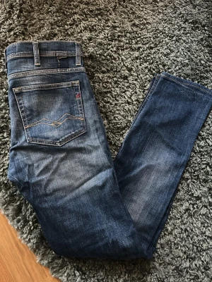 Replay jeans blåa - Säljer ett par klassiska blå jeans från Replay med snygga slitningar och kontrastsömmar på bakfickan. Jeansen har normal passform och är tillverkade i mjukt denimtyg med skön känsla. Perfekta till din vardagsstil!