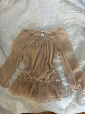 Ljus rosa blus med volang från Vero Moda - Söt ljus rosa blus från Vero Moda i tunn, luftig chiffong med bred volangkant nedtill. Blusen har rundad halsringning och fina veck framtill som ger en avslappnad men feminin look. Perfekt att styla med jeans eller kjol.