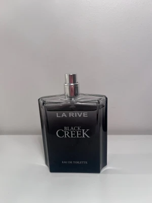 La Rive Black Creek Eau de Toilette - La Rive Black Creek Eau de Toilette med en stilren, svart glasflaska och silverfärgad spray. Flaskan har en modern, kantig form och text i vitt. Perfekt för dig som gillar eleganta och maskulina dofter. Endast använd få gånger