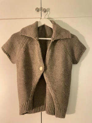 Zara brun stickad kofta med kort ärm - Stickad brun kofta med korta ärmar och stor krage. Koftan har en enkel knapp framtill och ribbstickade muddar vid ärmslut och nederkant. Perfekt att slänga över en t-shirt för en chill look.