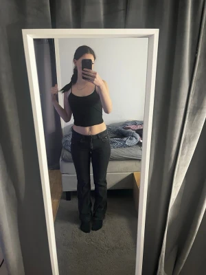 Svarta bootcut jeans med låg midja - Säljer ett par svarta bootcut jeans med låg midja. Jeansen har klassisk femficksdesign och raka ben som blir vidare nedtill. Perfekta för dig som gillar en tidlös och snygg look. Materialet är jeans i bomull.