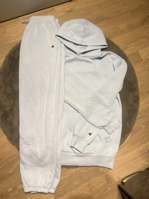 Baby blå  hoodie från Champion med huva - Säljer en stilren baby blå  hoodie från Champion med klassisk huva och magficka. Champion-loggan sitter diskret på ärmen och en liten etikett finns vid fickan. Hoodien har ribbade muddar vid ärmslut och nederkant. Perfekt för en avslappnad och sportig look.