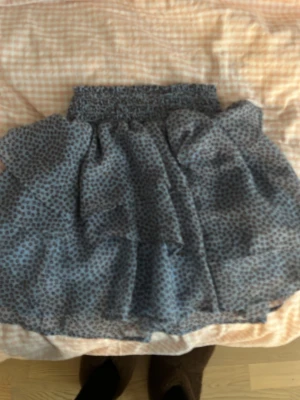 Blå leopardmönstrad kjol H&M - Söt blå kortkjol från H&M med leopardmönster och bred resår i midjan. Kjolen har ett lätt och luftigt tyg med volangig känsla, perfekt för en trendig och avslappnad stil.