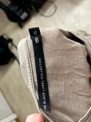 Beige t-shirt från The Black Label - Snygg beige t-shirt från The Black Label Collection i avslappnad passform. T-shirten har korta ärmar och är tillverkad i mjuk bomull, perfekt för en chill och stilren look. Diskret broderad logga på bröstet ger en clean vibe.