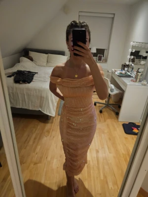 Glittrig offshoulder klänning - Säljer en glittrig, ljus champagnefärgad offshoulder-klänning med figurnära passform. Klänningen har omlott-detalj upptill och är axelbandslös, perfekt för dig som vill sticka ut. Materialet känns mjukt och stretchigt.