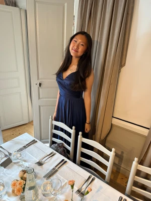 Balklänning - Elegant marinblå långklänning i glansigt satinmaterial med v-ringad omlottdesign och smala axelband. Kjolen faller mjukt och ger en lyxig känsla, perfekt för bal eller fest. Enkel men stilren look som verkligen sticker ut. Det finns inbyggd bh och öppen rygg med snören🩷storlek 10 passar mig som bär M/38 och längden passar bra på mig som är 174 + klackar🩷 använd en gång på balen i somras🩷nypris 3300 kr, priset går att diskutera🩷