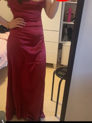 Vinröd långklänning med blom remsor - Elegant vinröd långklänning med blommor i remsor-design och figurnära passform. Klänningen har en mjuk, glansig yta och markerad midja som framhäver siluetten. Perfekt för speciella tillfällen. PRIS KAN DISKUTERAS! Köpte den för 299kr