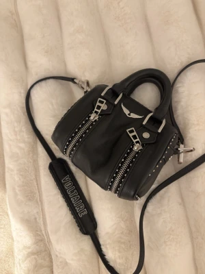 Svart handväska Zadig & Voltaire skinn - Cool svart handväska i skinn från Zadig & Voltaire med dubbla dragkedjor framtill, silverdetaljer och ikoniska vingar. Väskan har både handtag och justerbar axelrem med logga. Ny pris 2200