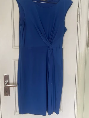 Blå omlottklänning från Esprit - Snygg blå kortklänning från Esprit med omlottdetalj framtill och rund halsringning. Klänningen har en elegant drapering och är ärmlös, vilket ger en stilren och modern look. Perfekt för dig som vill ha en enkel men chic outfit. Superfin till sommaren💕