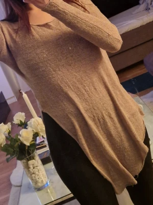 Beige asymmetrisk långärmad tröja - Säljer en beige långärmad tröja med asymmetrisk nederkant. Tröjan har en mjuk och tunn stickning, rund halsringning och sitter löst på kroppen. Perfekt för dig som gillar en avslappnad och trendig stil.