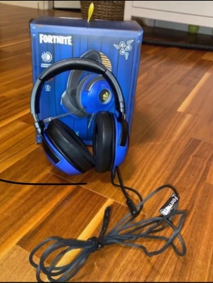 Razer Fortnite blå gaming headset - Säljer ett blått Razer Fortnite gaming headset med over-ear design och mjuka svarta öronkuddar. Headsetet har kabelanslutning och inbyggd mikrofon, perfekt för gaming och voice chat. Snygg Fortnite-design soppar upplevelsen till nästa nivå. Fanns en kod till headsetet men är tyvärr använd. Passar till dator och PlayStation (se bild 6). Ordinarie pris: 1499kr