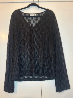 Svart meshblus med glitter - Snygg svart meshblus från VILA med transparent material och glittrigt mönster. Blusen har v-ringning och långa lite utsvängda ärmar. Perfekt för utgång eller när man vill vara lite finare! Endast använd fåtal gånger🫶🏻