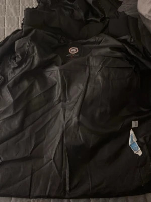 Svart dunjacka från Canada Goose - Säljer en svart dunjacka från Canada Goose med huva och klassisk logga på ärmen. Jackan har dragkedja, stora fickor framtill och är perfekt för kalla dagar. Stilsäker och varm modell som funkar till det mesta. Finns ett hål men de syns inte så mycke när man har på sig den🙂 